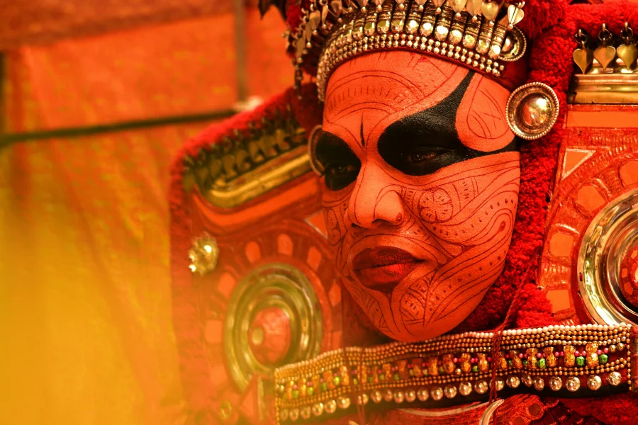 Close-up of a Theyyam performer in vibrant red traditional makeup and intricate ornaments during a ritualistic dance performance in Varanasi