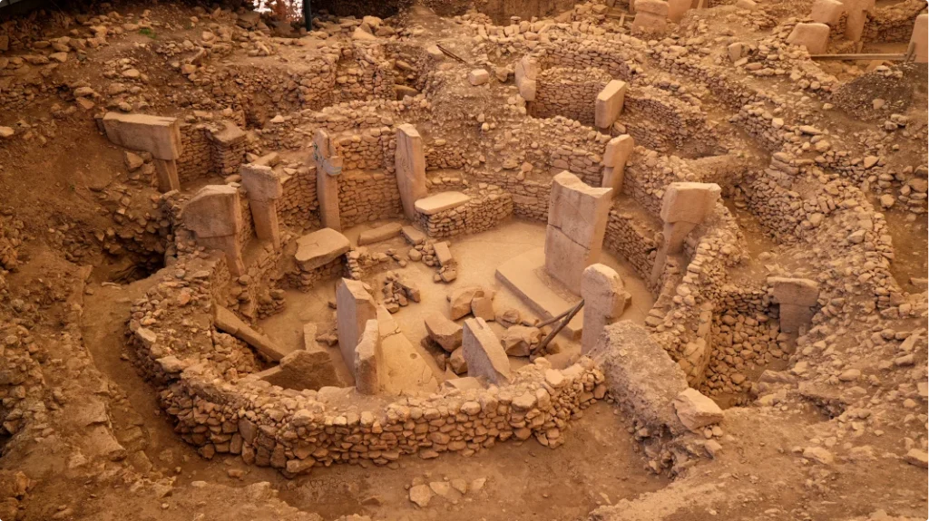 A view of Göbekli Tepe, the ancient archaeological site in Turkey, featuring intricately carved T-shaped stone pillars dating back over 11,000 years, set against a rugged landscape, symbolizing one of humanity's earliest known temples