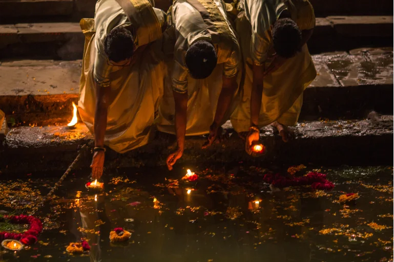 Three Hindu devotees releasing lit candles into the sacred waters of the Ganges River during a spiritual ritual, symbolizing devotion, purification, and prayers for blessings