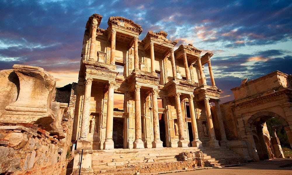 The Library of Celsus in Ephesus, Turkey, illuminated by warm sunlight during a dramatic sunset, with ancient columns and intricate carvings showcasing Roman architecture and history.
