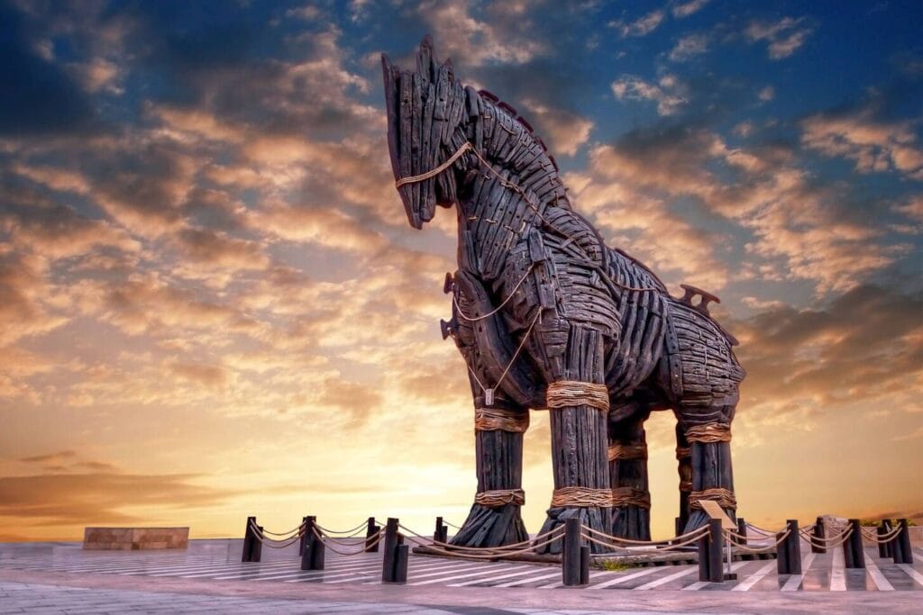 The iconic wooden Trojan Horse sculpture in the ancient city of Troy, Turkey, standing under a vivid sky blending shades of blue and orange during sunset, symbolizing the legendary tale of the Trojan War
